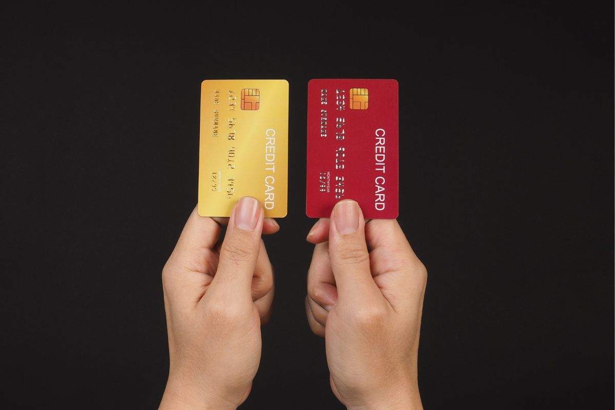 two hands holding a debit card and a credit card side by side